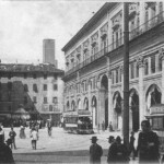 Immagine da cartolina d'epoca. Piazza Uccelli si trovava tra il lato orientale di Palazzo del Podestà e il portico di Palazzo dei Banchi. Dietro si intravede la torre Lambertini ed i i merli restaurati del Palazzo del Podestà. Gli stabili che si trovavano tra questa piazza e via Rizzoli (isolati che comprendevano via Accuse e via Spaderie) furono definitivamente abbattuti nel 1913.